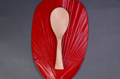 hand carved wooden rice paddle light golden brown yellowish tone of paddle atop deep red background surface
