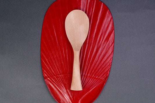hand carved wooden rice paddle light golden brown yellowish tone of paddle atop deep red background surface