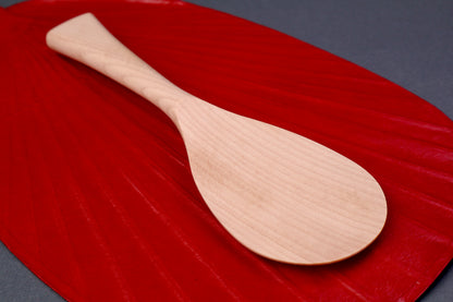 hand carved wooden rice paddle light golden brown yellowish tone of paddle atop deep red background surface