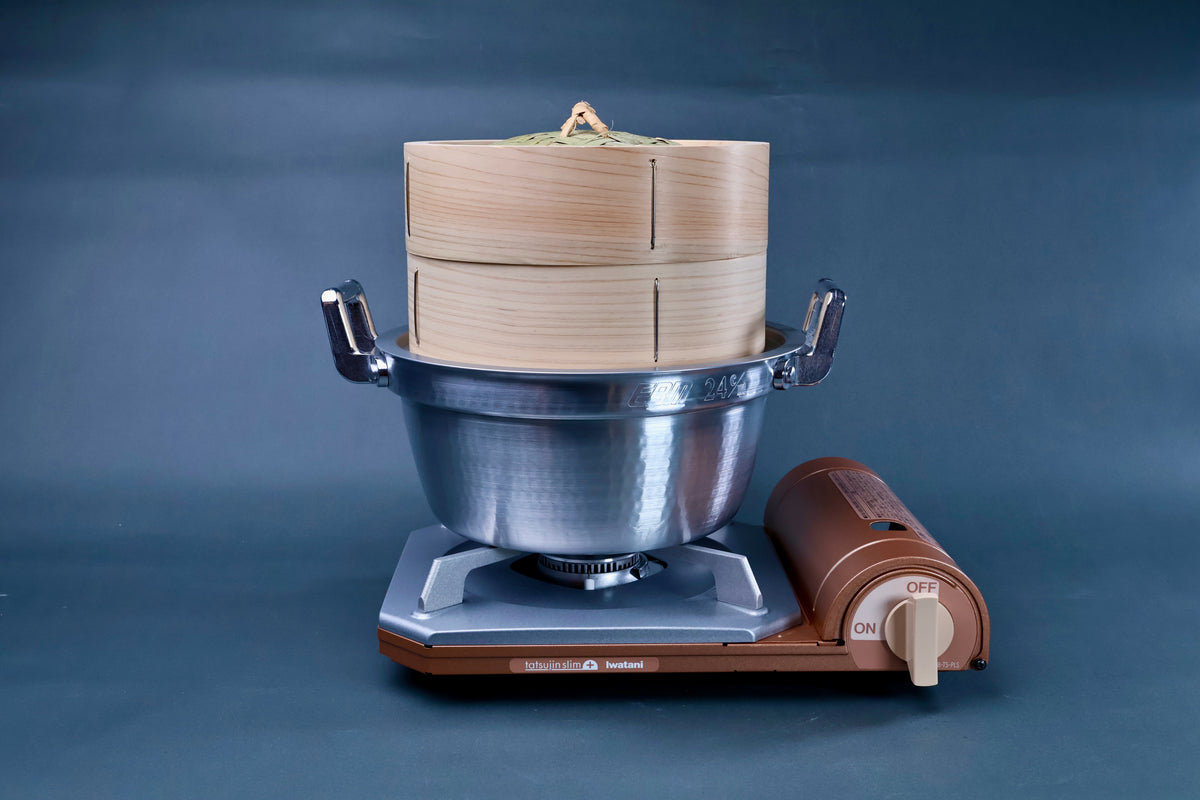Bamboo steamer kit 21cm assembled on Iwatani portable gas burner showing cedar steamer body in aluminum pot on blue background