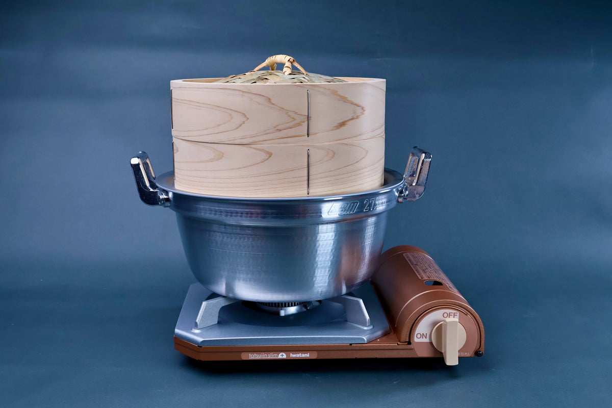 Bamboo steamer kit 24cm assembled on Iwatani portable gas burner showing cedar wood grain and aluminum pot on blue background