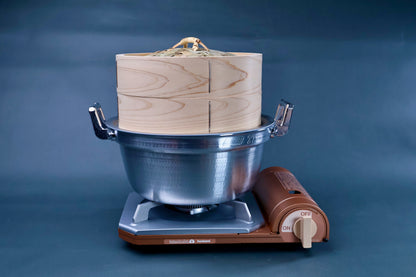 Bamboo steamer kit 24cm assembled on Iwatani portable gas burner showing cedar wood grain and aluminum pot on blue background