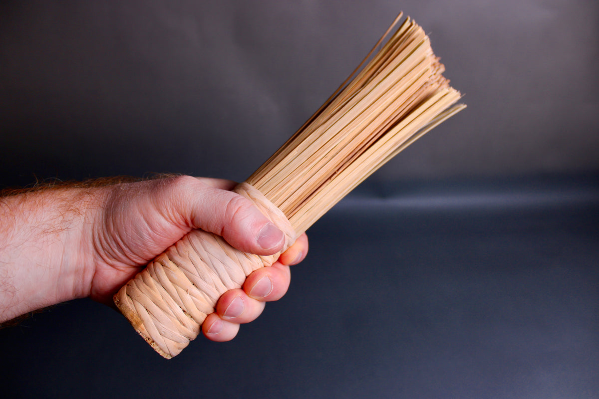 hand holding wide short woven bamboo brush thick sturdy beveled edge atop dark grey background