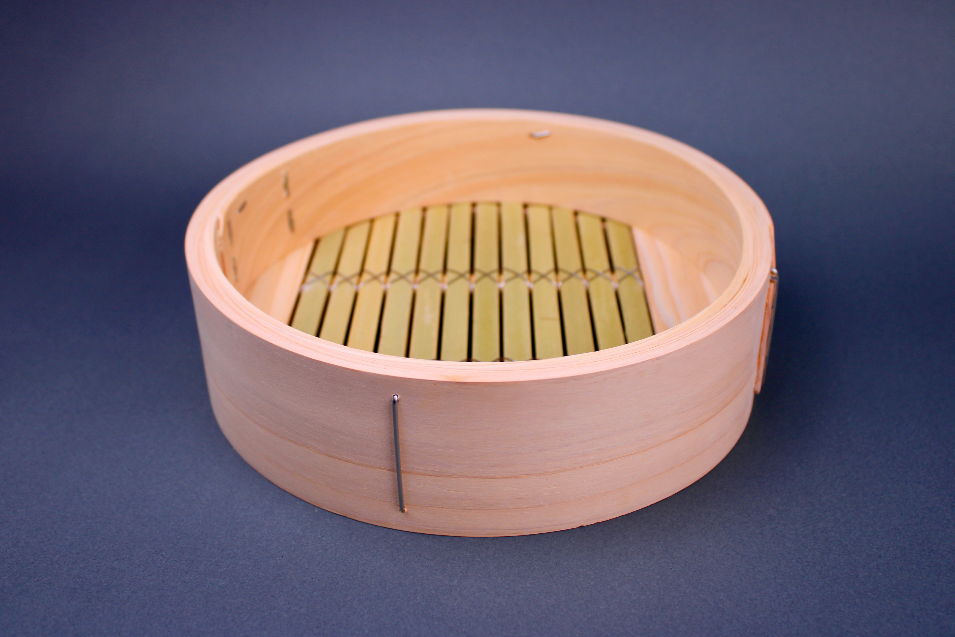 round thick hinoki wood bamboo steamer base with thick greenish slats interior surrounded by japanese kitchenware on blue gray surface