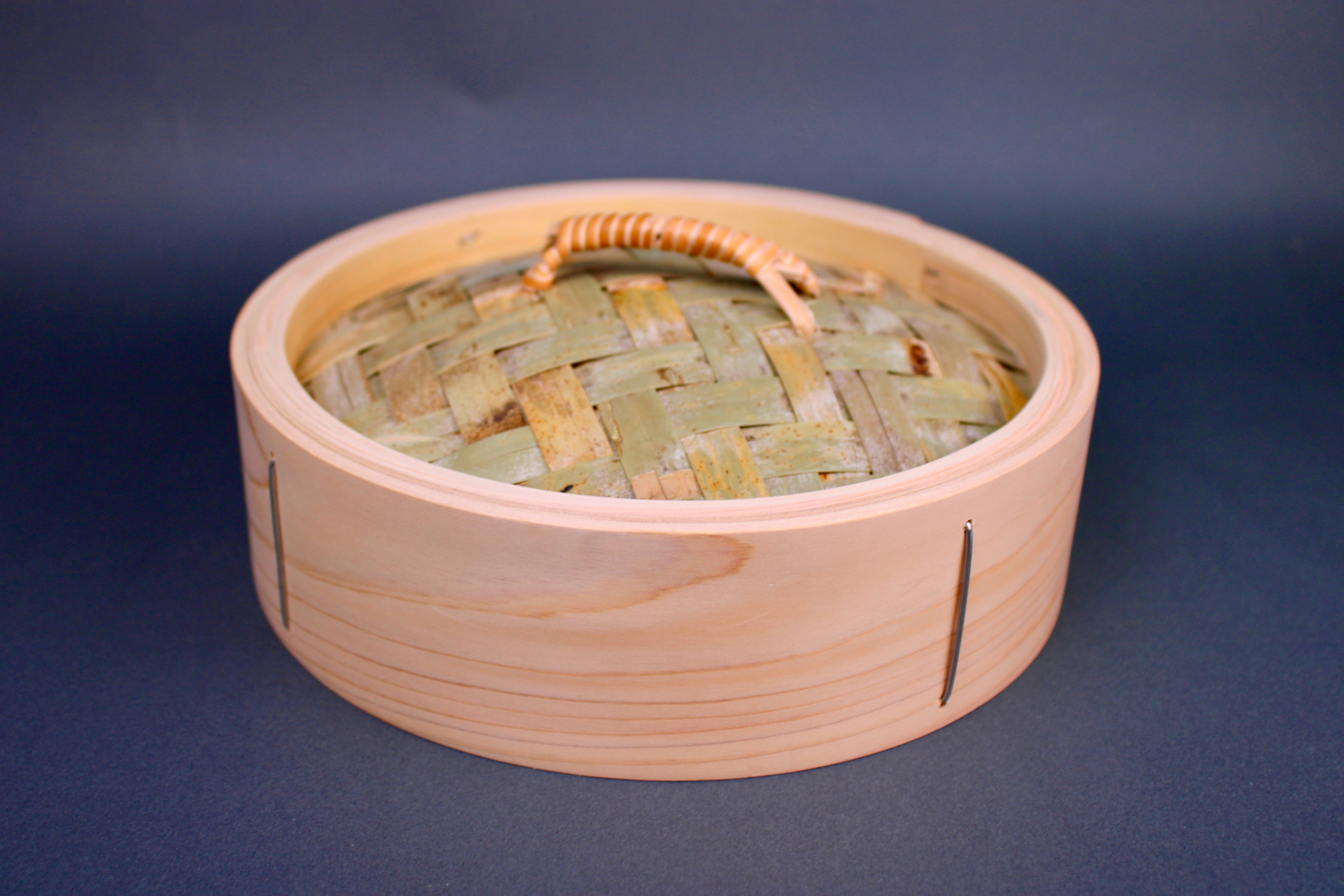 bamboo steamer lid woven bamboo with looped handle surrounded by thick hinoki wood exterior on gray surface