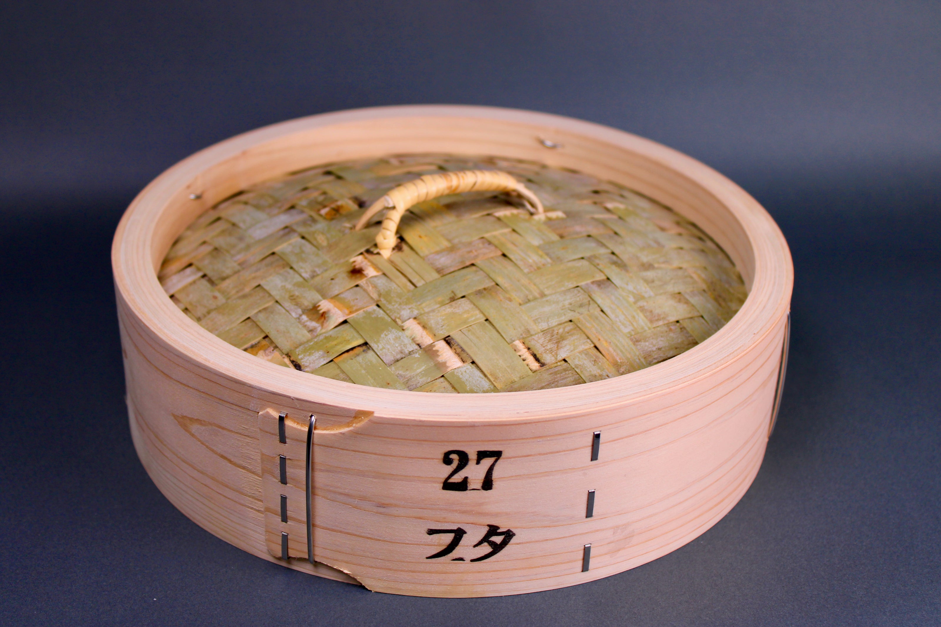 bamboo steamer lid woven bamboo with looped handle surrounded by thick hinoki wood exterior on gray surface