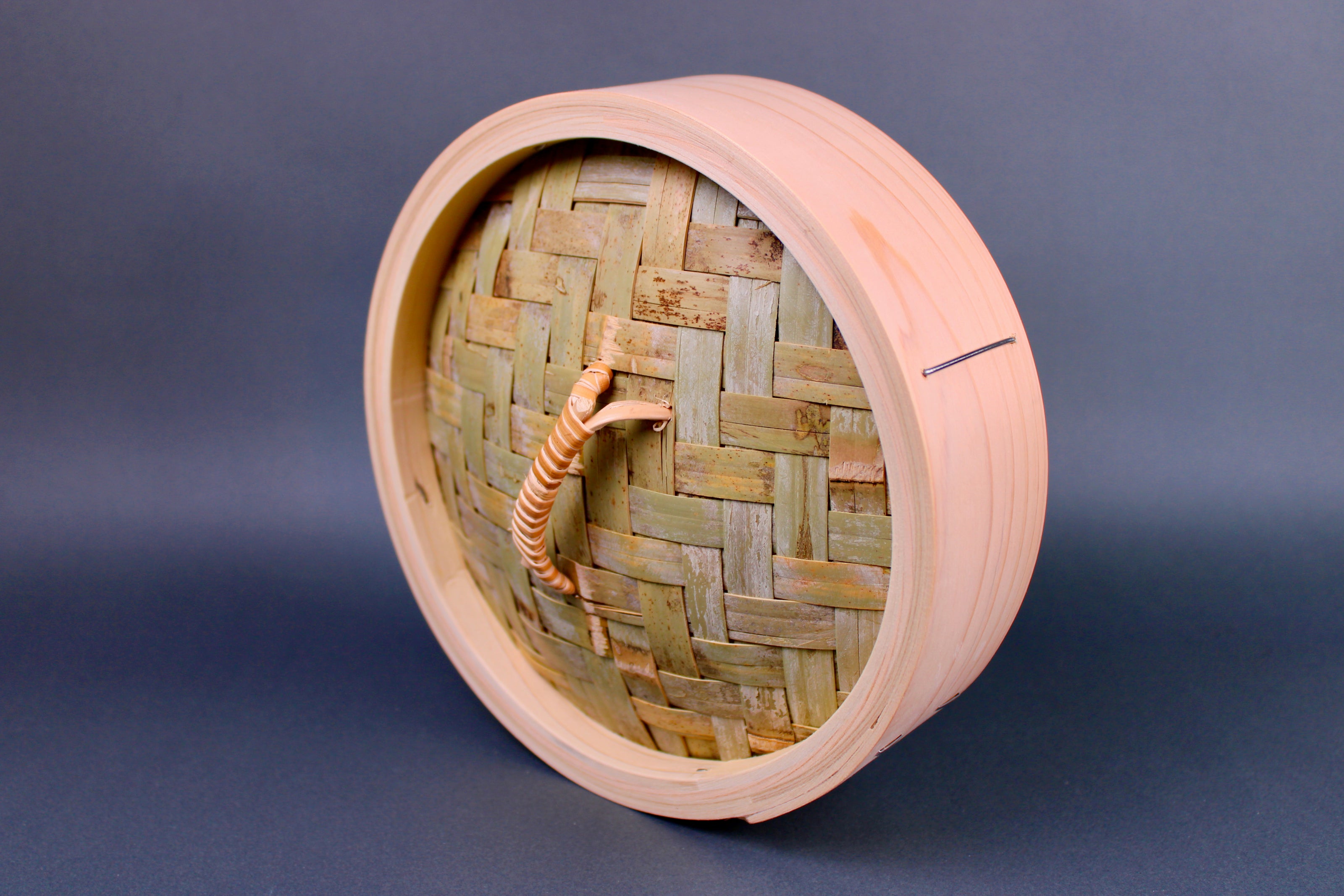 bamboo steamer lid woven bamboo with looped handle surrounded by thick hinoki wood exterior on gray surface