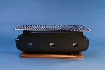Banko yaki konro grill front profile showing black ceramic body with three ventilation holes, stainless wire grill and wood base on blue background