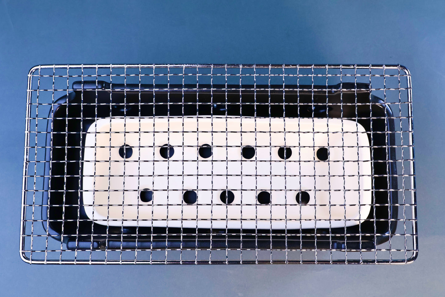 Banko yaki konro grill overhead view showing stainless wire grill over white ceramic fire plate with ventilation holes on blue background