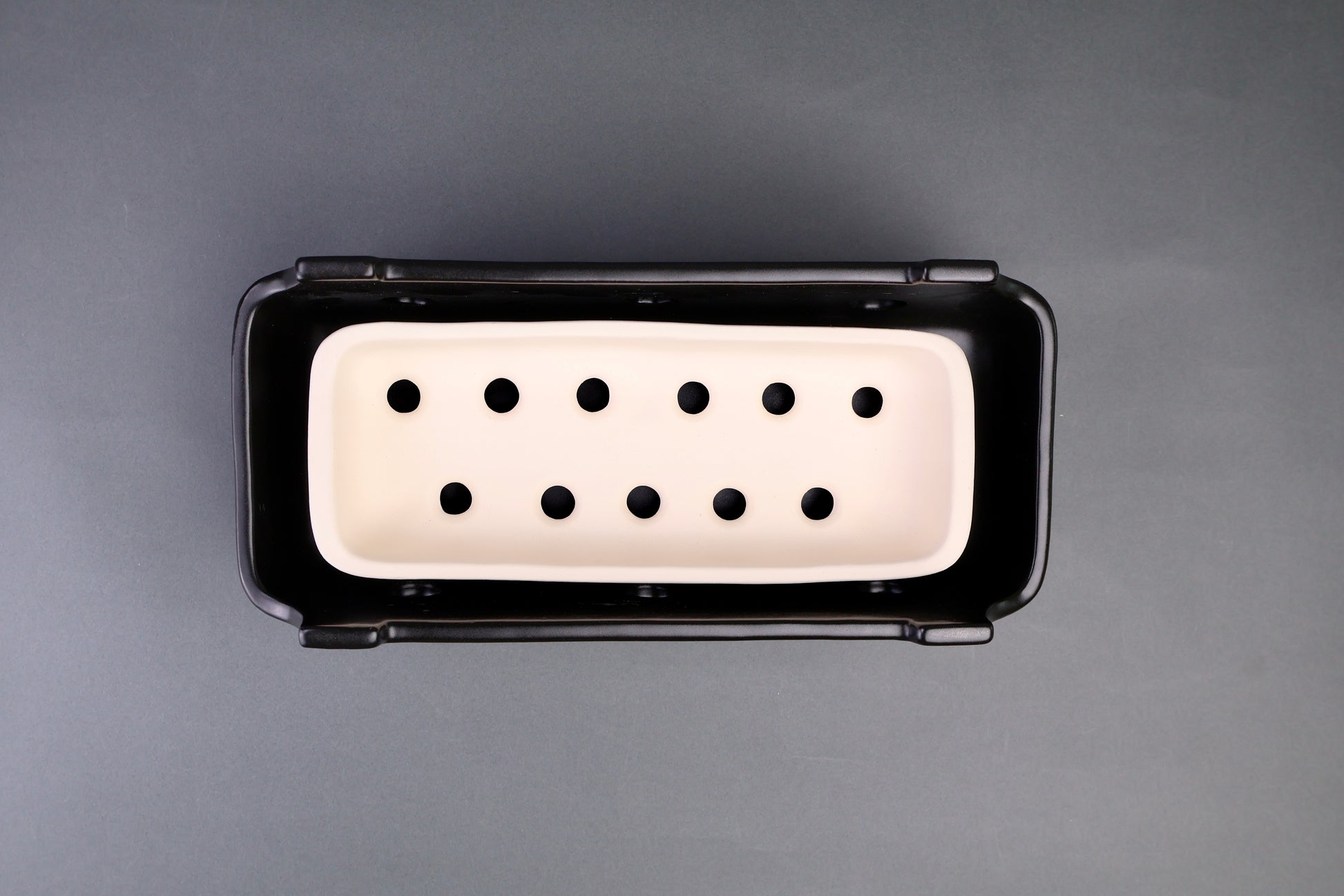 black glazed rectangular ceramic grill outer body with white unglazed interior charcoal tray in grey background