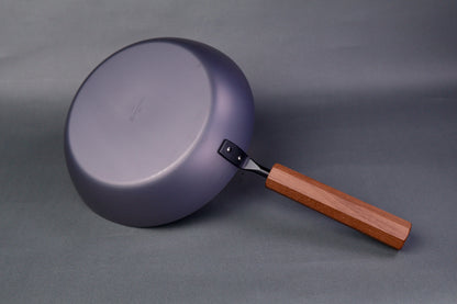 underside of wide low bluish grey black carbon steel saute pan octagonal wood handle in grey background
