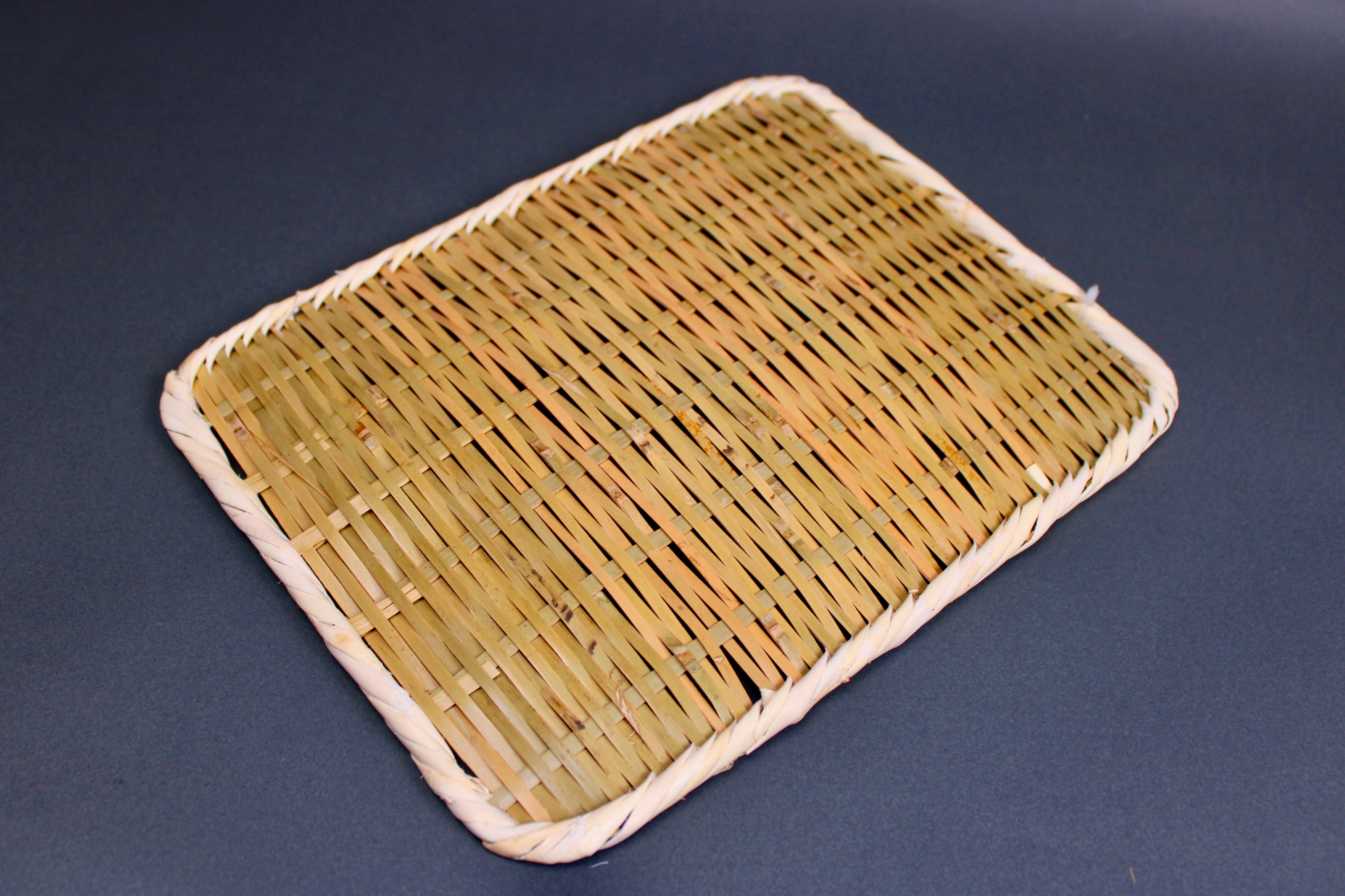 woven bamboo strainer rectangular tan brownish in color with  grey blue backdrop