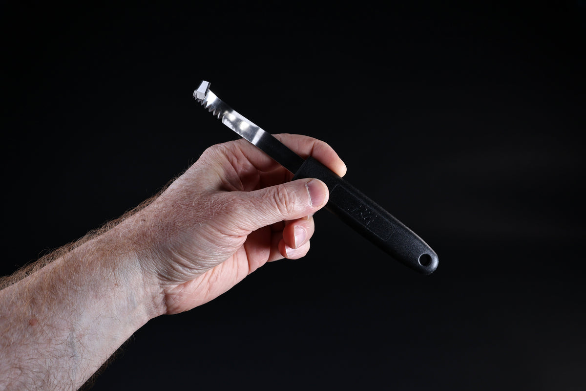 Butter curler and vegetable tool — blade face, serrated teeth, and handle grip shown from reverse angle in hand