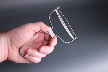 detail shot of hand holding large metal vegetable peeler with the words stainless steel imprinted made in japan grey background 