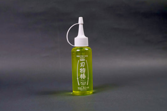 clear plastic dispenser bottle with white tipped cap containing yellowish gold oil with hiragana writing and sword animation in grey backdrop