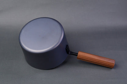  underside of dark grey carbon steel tall narrow iron saucepan with octagonal deep brown wood handle in light grey background