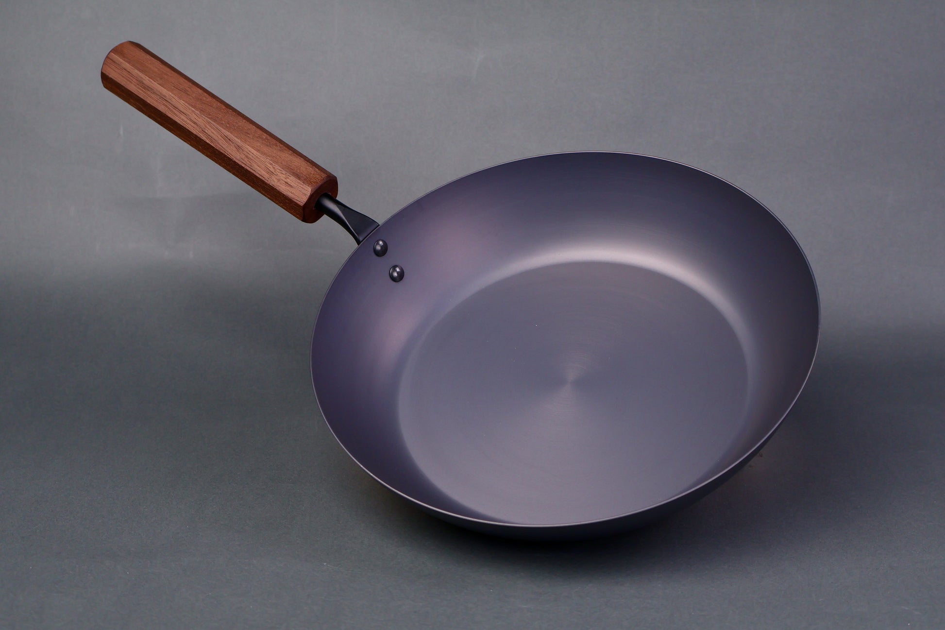 wide low bluish grey black carbon steel saute pan octagonal wood handle in grey background