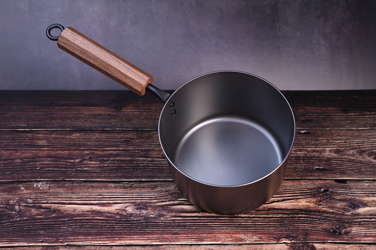 Carbon Steel Nitride saucepan 16cm showing dark interior and walnut handle with hanging ring on wood surface
