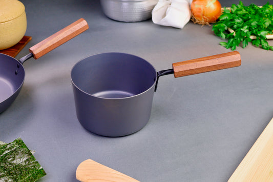 closeup shot of iron rust free saucepan surrounded by kitchenware grey background