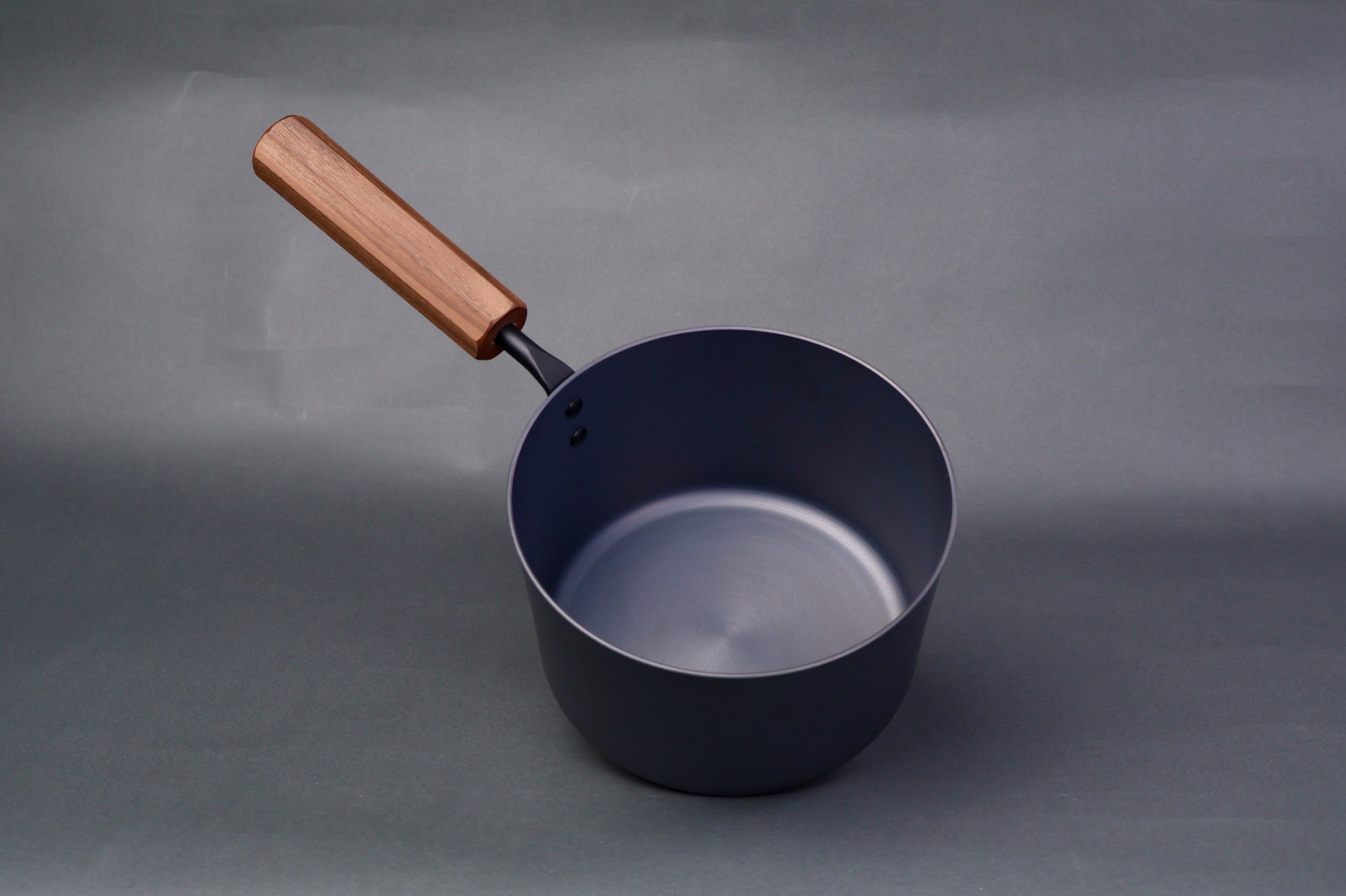 dark grey carbon steel tall narrow iron saucepan with octagonal deep brown wood handle in light grey background
