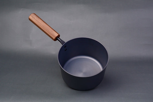 dark grey carbon steel tall narrow iron saucepan with octagonal deep brown wood handle in light grey background