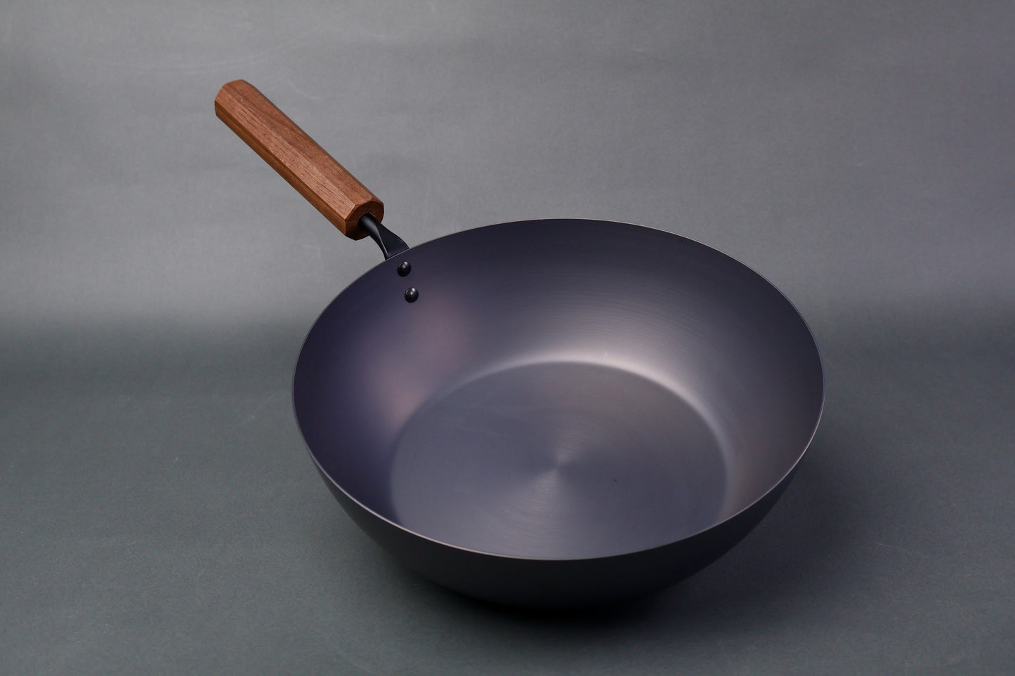 wide deep bluish black carbon steel pan long octagonal wood handle in light grey backdrop