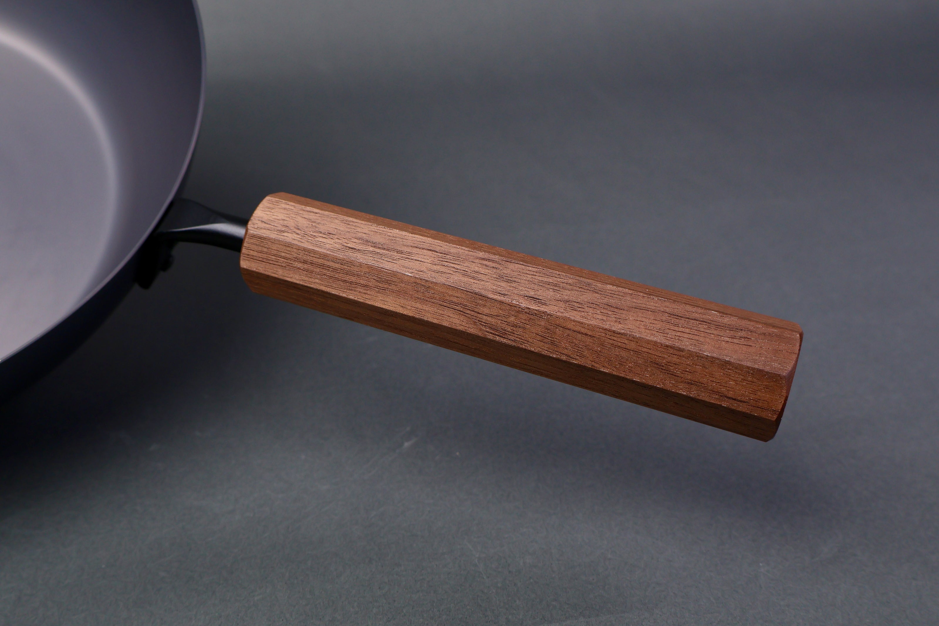 close up shot of wooden octagonal handle for carbon steel pan in grey background
