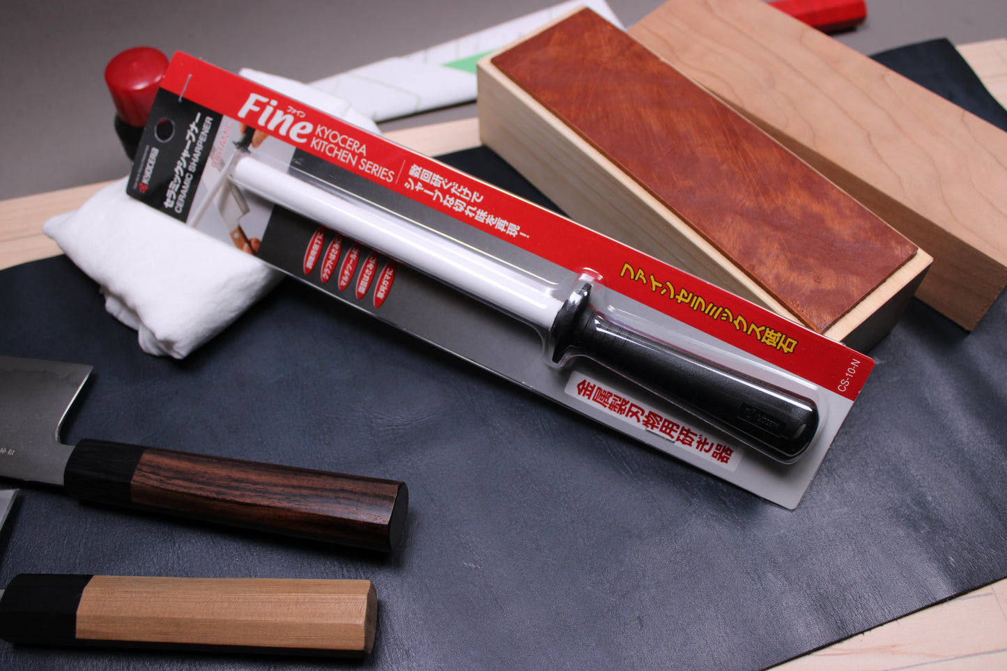  honing rod in package labeled fine kyocera kitchen series near leather knife strop and two japanese knives