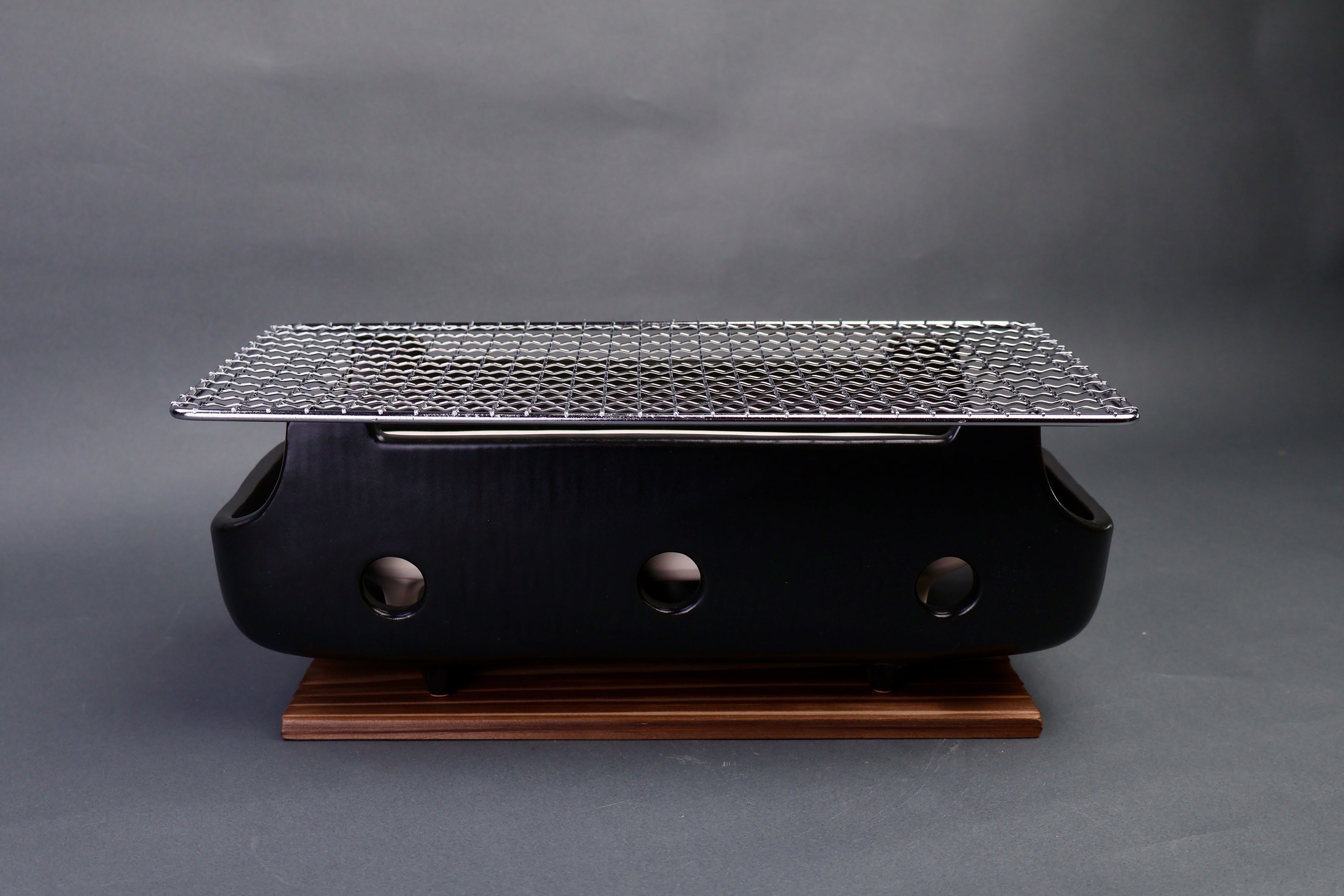 long back ceramic rectangular charcoal grill white tray interior stainless steel grill grate atop tan wood trivet in gray surrounding 