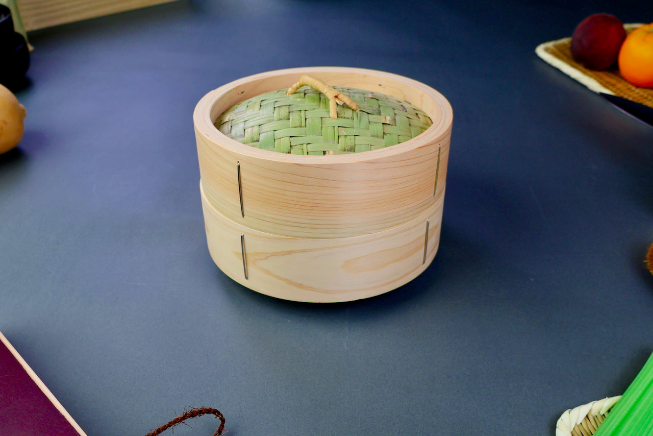 Wooden steamer basket with a woven lid on a blue surface