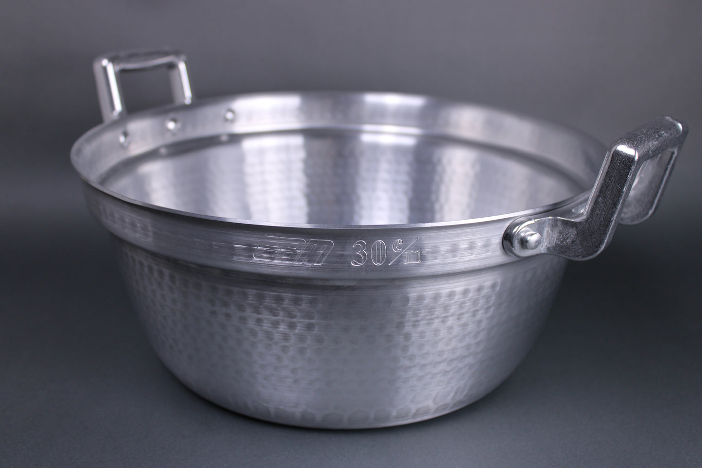 closeup shot of aluminum pot with two large handles and an inner ledge for accommodating steamers the surface is textured from hammering technique and blends into grey background