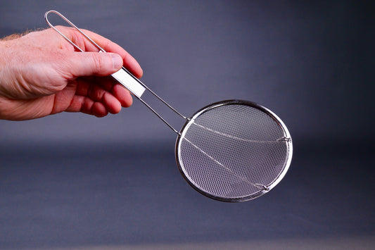 Metal coarse skimmer with long thin handle held by a hand against a dark background