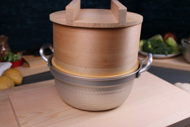 detail shot of dantsuki steaming pot with round handmade hinoki wood steaming basket sitting on top with wood lid and handle with kitchen background showing japanese cookware