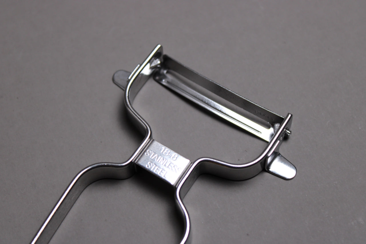 stainless steel vegetable peeler with curved blade wide grip shown on grey background closeup of blade