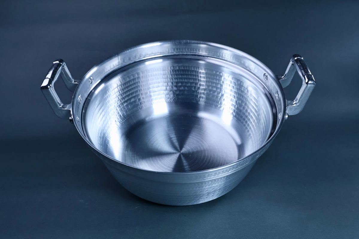 Dantsuki seiro pot 30cm angled view showing hammered aluminum interior and wide rim with chrome handles on blue-grey background