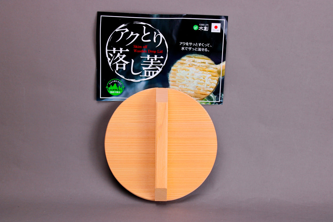 circular wood drop lid with long shallow handle yellowish gold hue beside black product tag with hiragana in front of grey background