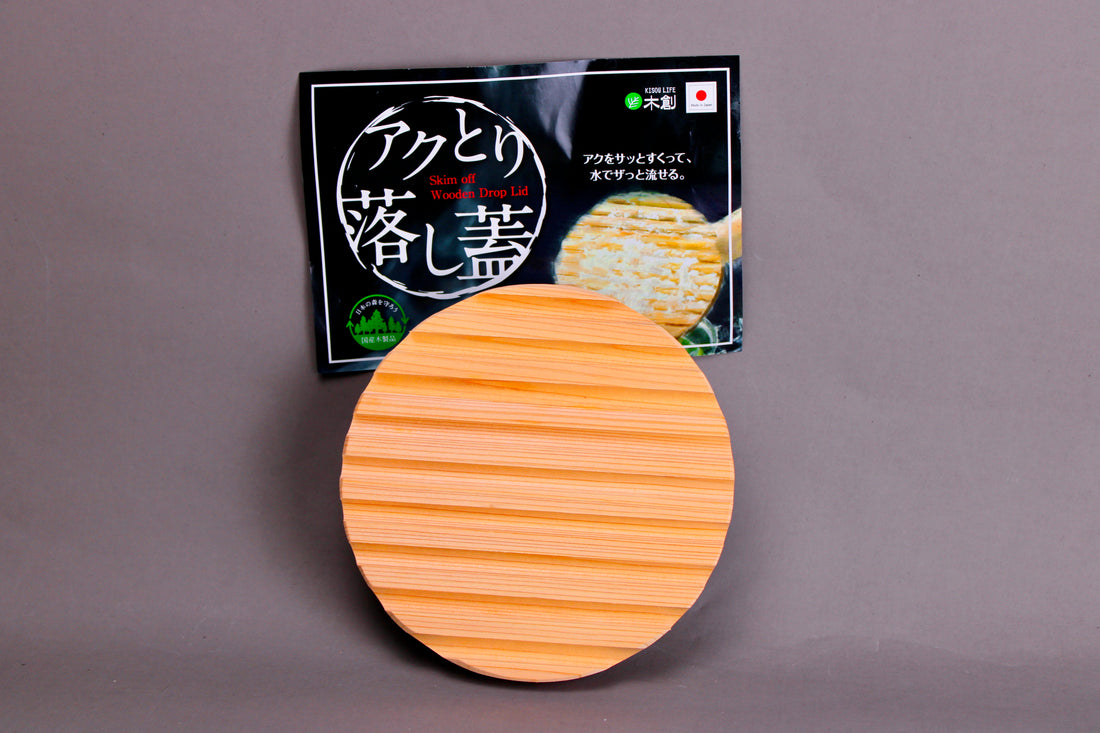 back side with ridges circular wood drop lid with long shallow handle yellowish gold hue beside black product tag with hiragana in front of grey background