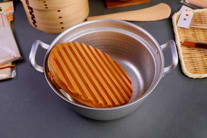 interior of hammered two handled pot with wooden drop lid inside with ridges surrounding kitchenware on dark grey background