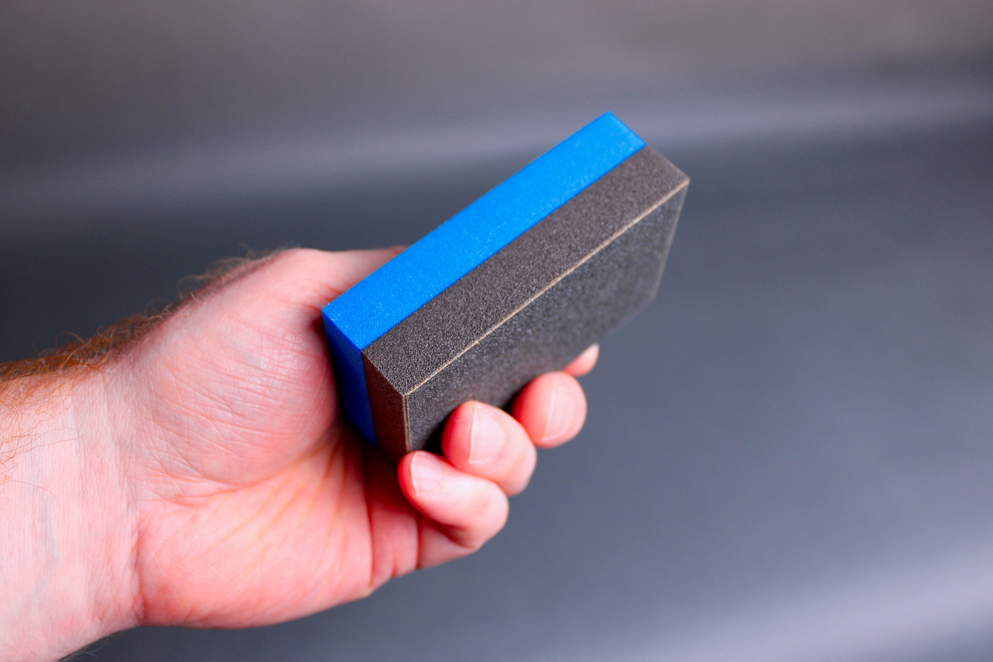 hand holding rectangular half black half blue cutting board scrapper with grey background