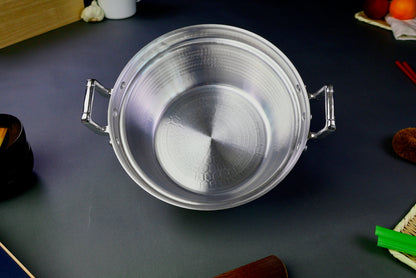 interior of two handled stepped aluminum silvery pot surrounded by japanese kitchenware on a dark grey backdrop 