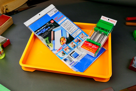 Orange knife sharpening box with a blue hasegawa non slip mat and green whetstone holder kit on a gray surface
