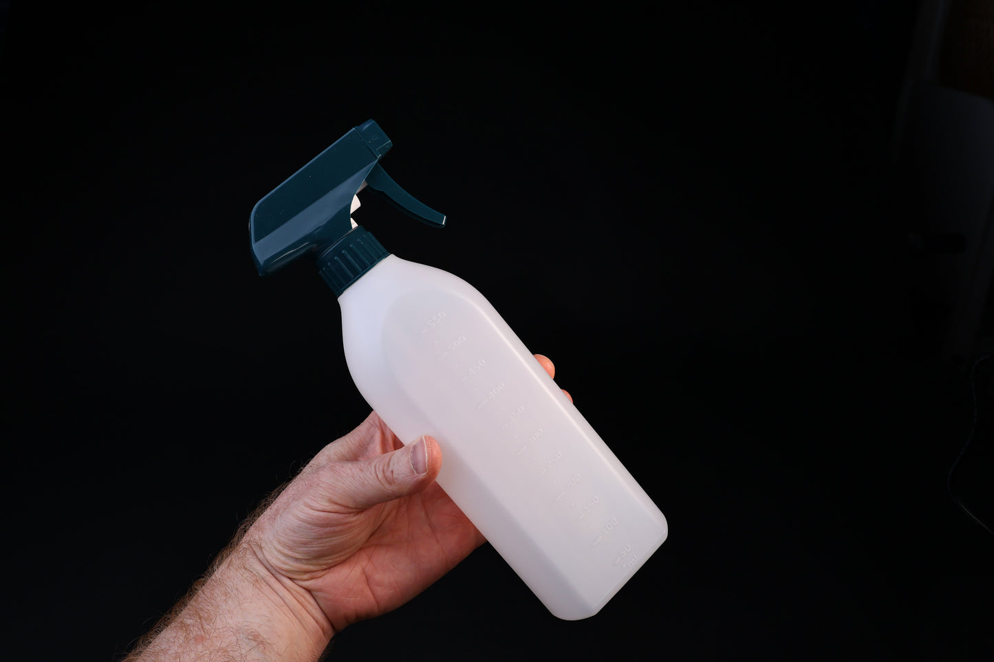 Flat-sided spray bottle held in hand showing size, teal trigger head and volume markings on white bottle