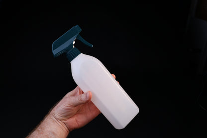 Flat-sided spray bottle held in hand showing size, teal trigger head and volume markings on white bottle
