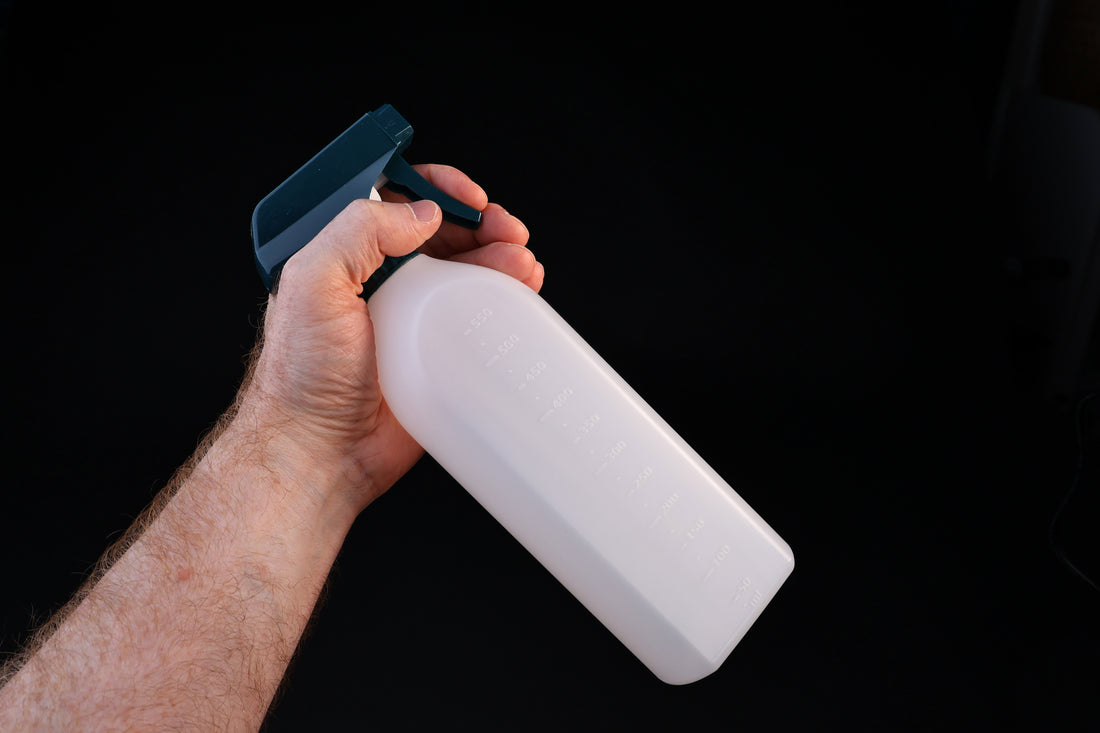Flat-sided spray bottle held in trigger grip position showing teal spray head and measured bottle body
