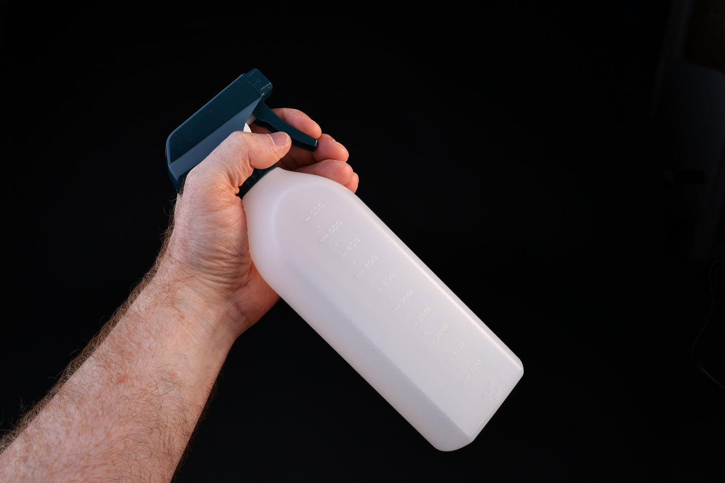 Flat-sided spray bottle held in trigger grip position showing teal spray head and measured bottle body