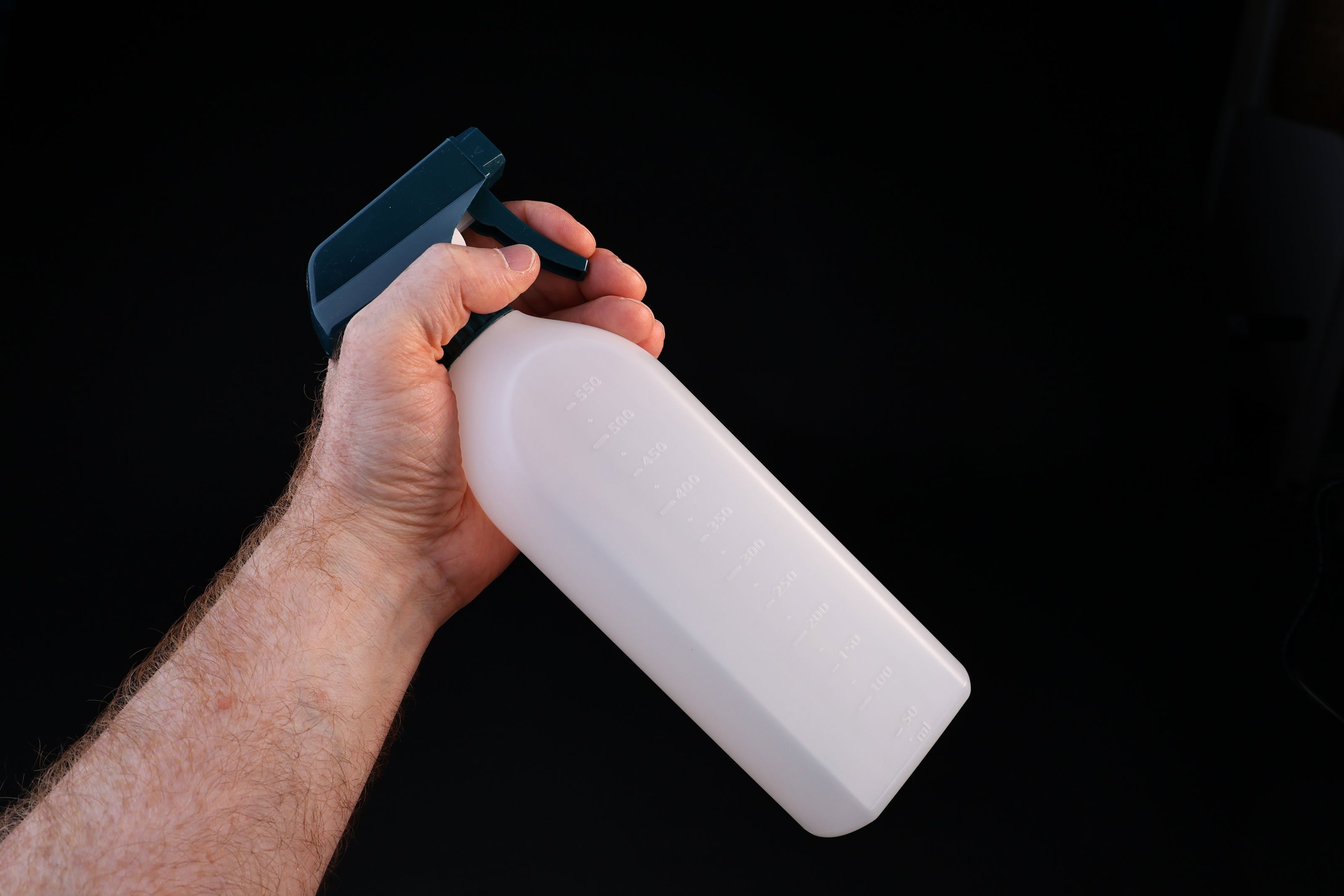Flat-sided spray bottle held in trigger grip position showing teal spray head and measured bottle body