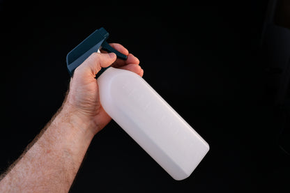 Flat-sided spray bottle held in trigger grip position showing teal spray head and measured bottle body