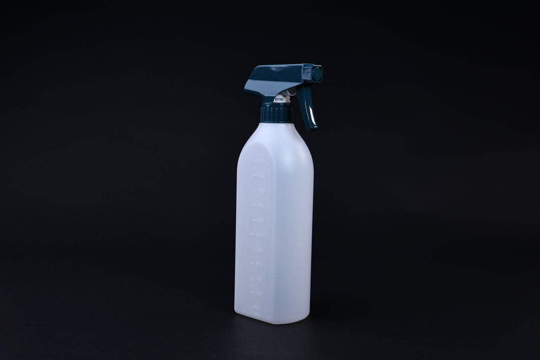 Flat-sided spray bottle standing upright on black background, teal trigger head and embossed volume markings
