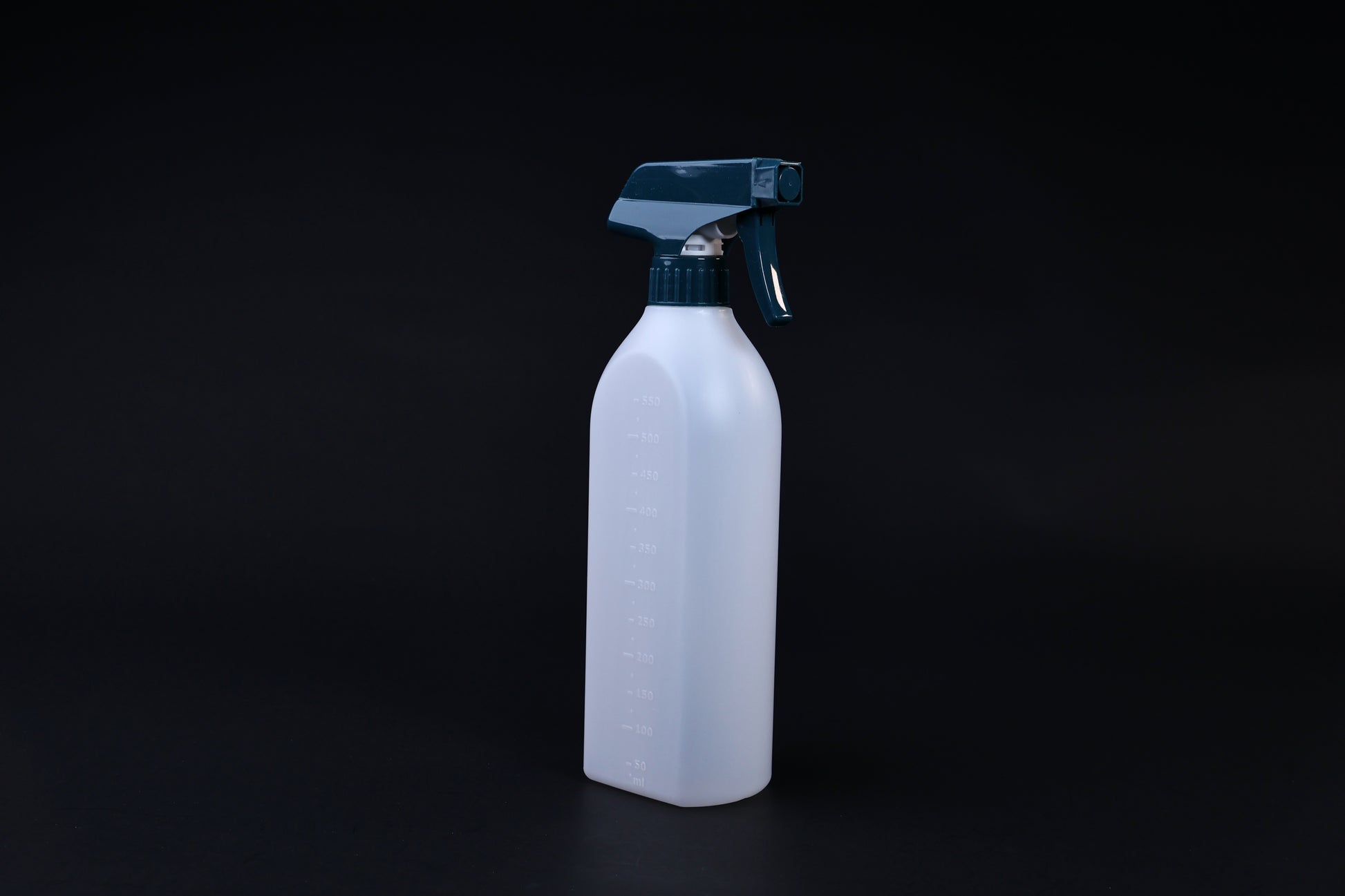 Flat-sided spray bottle standing upright on black background, teal trigger head and embossed volume markings