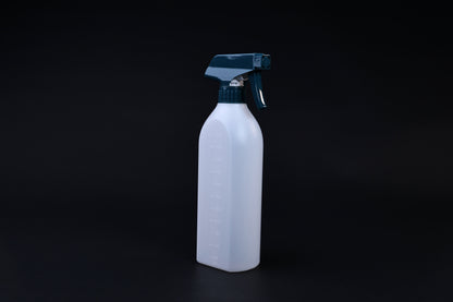 Flat-sided spray bottle standing upright on black background, teal trigger head and embossed volume markings